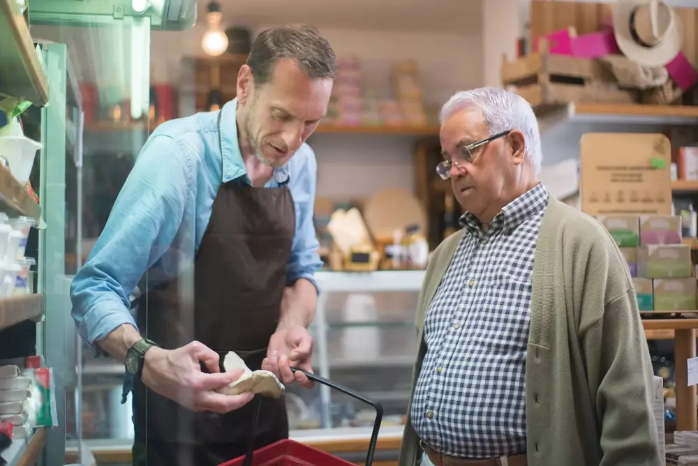 Tendero atendiendo con cariño a un cliente mayor en su tienda de barrio